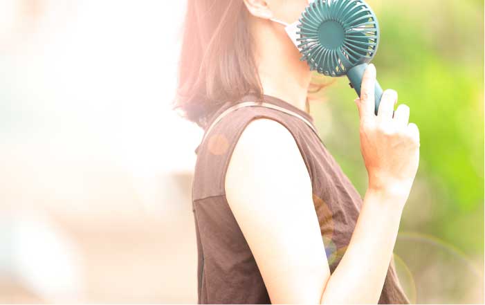 ハンディファンで涼みながら暑さをしのぐ女性